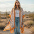 Woman in a desert setting wearing an orange patterned kimono, white top, and blue jeans.