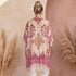 A woman viewed from behind wearing a loose pink kimono with pink and gold floral embroidery, standing in front of a textured pink wall with pampas grass decor.