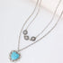 A double-strand silver-tone necklace featuring a heart-shaped turquoise pendant on one chain and three small sunburst medallions on the other, displayed on a clean white background.